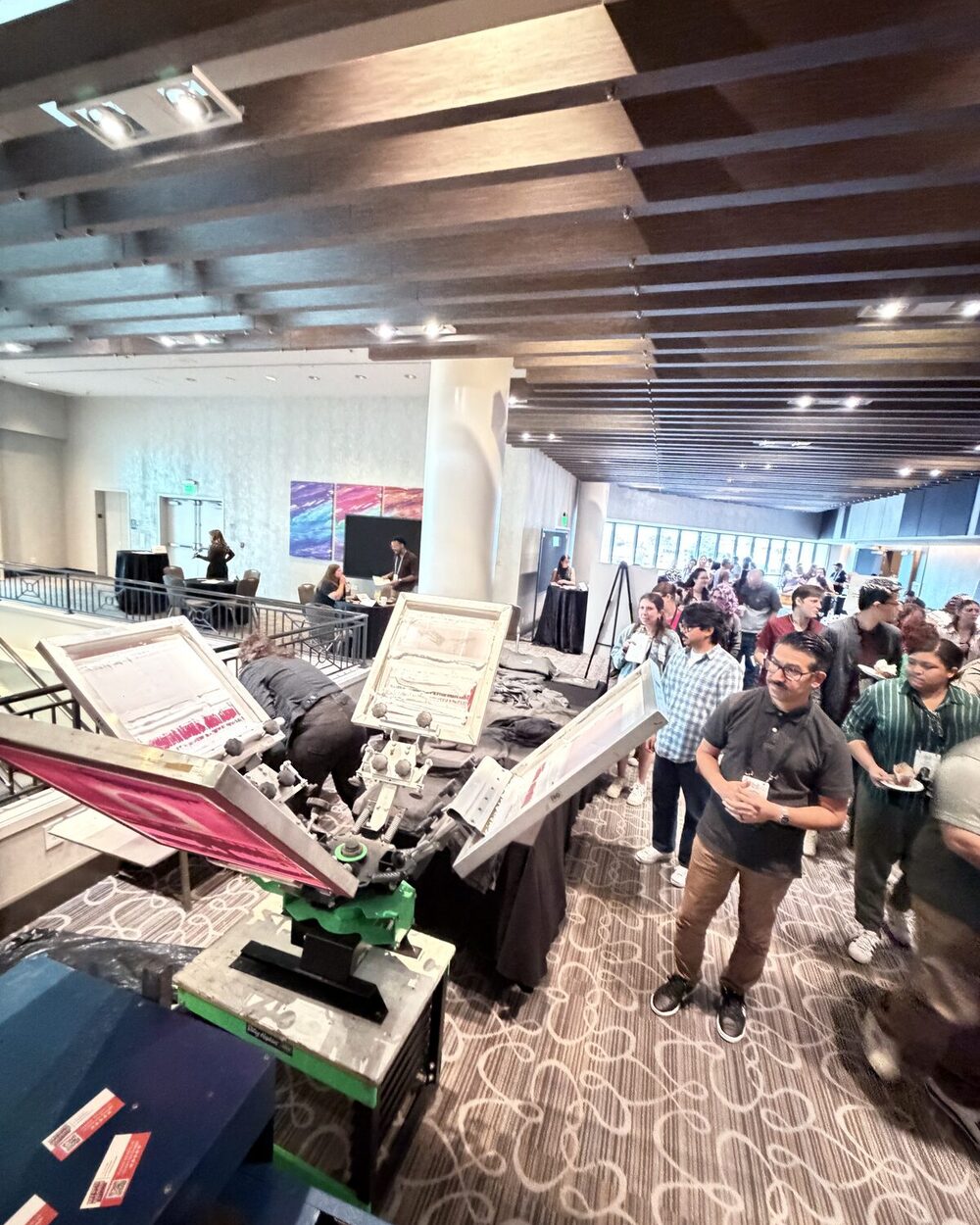 Conference attendees watching a manual screen printing carousel on a mezzanine level